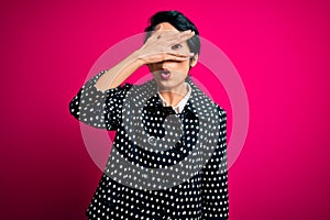 Young beautiful asian girl wearing casual jacket standing over isolated pink background peeking in shock covering face and eyes