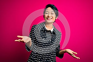 Young beautiful asian girl wearing casual jacket standing over isolated pink background smiling cheerful with open arms as