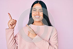 Young beautiful asian girl wearing casual pink sweater smiling and looking at the camera pointing with two hands and fingers to
