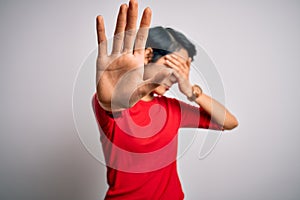 Young beautiful asian girl wearing casual red t-shirt standing over isolated white background covering eyes with hands and doing