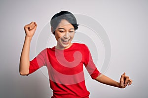 Young beautiful asian girl wearing casual red t-shirt standing over isolated white background Dancing happy and cheerful, smiling