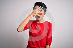 Young beautiful asian girl wearing casual red t-shirt standing over isolated white background peeking in shock covering face and