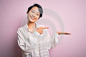 Young beautiful asian girl wearing casual shirt standing over isolated pink background amazed and smiling to the camera while