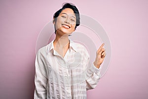 Young beautiful asian girl wearing casual shirt standing over isolated pink background with a big smile on face, pointing with