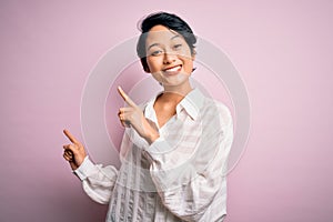 Young beautiful asian girl wearing casual shirt standing over isolated pink background smiling and looking at the camera pointing