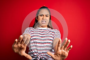 Young beautiful asian girl wearing casual striped t-shirt over isolated red background afraid and terrified with fear expression