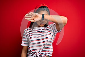 Young beautiful asian girl wearing casual striped t-shirt over isolated red background covering eyes with arm, looking serious and