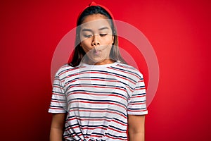 Young beautiful asian girl wearing casual striped t-shirt over isolated red background making fish face with lips, crazy and