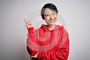 Young beautiful asian girl wearing casual sweatshirt with hoodie over white background with a big smile on face, pointing with