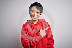 Young beautiful asian girl wearing casual sweatshirt with hoodie over white background cheerful with a smile of face pointing with