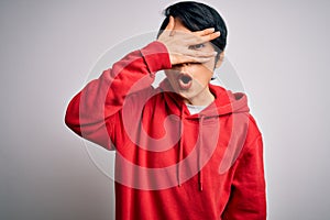 Young beautiful asian girl wearing casual sweatshirt with hoodie over white background peeking in shock covering face and eyes