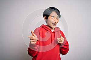 Young beautiful asian girl wearing casual sweatshirt with hoodie over white background pointing fingers to camera with happy and