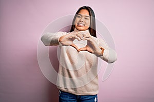 Young beautiful asian girl wearing casual turtleneck sweater over isolated pink background smiling in love doing heart symbol