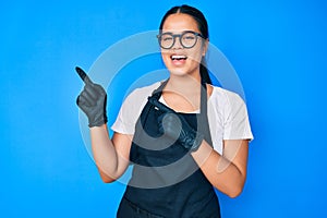 Young beautiful asian girl wearing professional apron smiling and looking at the camera pointing with two hands and fingers to the