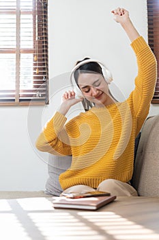 Young beautiful Asian girl in yellow shirt, happy carefree wearing headphones enjoying relaxing music
