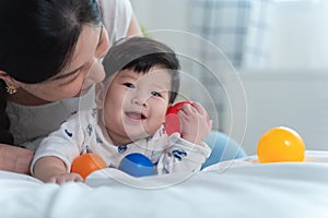 Giovane bellissimo asiatico madre asiatico un bambino sul un letto un giocattolo sfera comune su bianco un letto sensazione Contento un contento un 