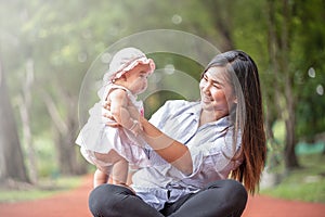 Young beautiful Asian mother smiling and  holding little baby girl in the park. Familiy having a happy time together