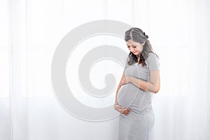Young beautiful Asian pregnant woman standing at home near the window