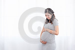 Young beautiful Asian pregnant woman standing at home near the window