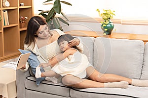 Young beautiful Asian pregnant women reading the book and her toddler daughter laying down having ear on mother tummy. Little girl