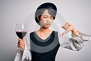 Young beautiful asian sommelier girl drinking glass of red wine over isolated white background with angry face, negative sign