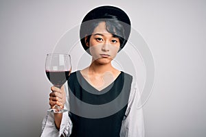 Young beautiful asian sommelier girl drinking glass of red wine over isolated white background with a confident expression on