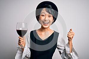 Young beautiful asian sommelier girl drinking glass of red wine over isolated white background screaming proud and celebrating