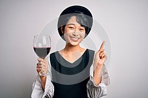 Young beautiful asian sommelier girl drinking glass of red wine over isolated white background surprised with an idea or question