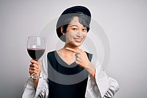 Young beautiful asian sommelier girl drinking glass of red wine over isolated white background very happy pointing with hand and