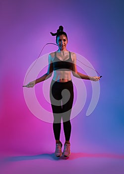 Young Beautiful Asian sports girl doing exercises with jumping rope in fitness studio neon background. Woman exercising with