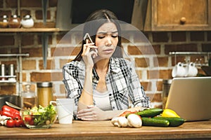 Young beautiful asian stressed woman with laptop on kitchen. Using phone. Working home. In stress.