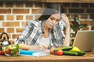 Young beautiful asian stressed woman with laptop on kitchen. Working home. In stress.