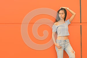 Young beautiful Asian teenage girl against orange wall