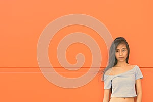 Young beautiful Asian teenage girl against orange wall