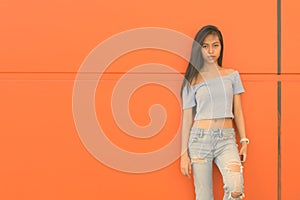 Young beautiful Asian teenage girl against orange wall