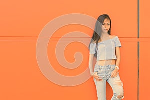 Young beautiful Asian teenage girl against orange wall