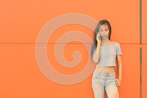 Young beautiful Asian teenage girl against orange wall