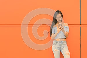 Young beautiful Asian teenage girl against orange wall