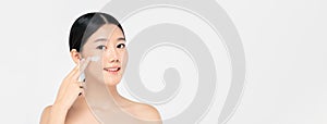 Young beautiful Asian woman applying cream to face on banner background