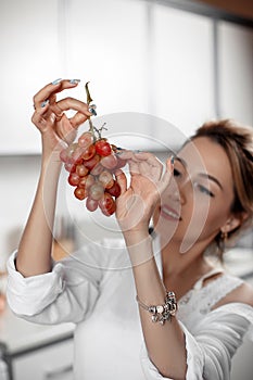 Young beautiful Asian woman in beige lace shorts,white shirt eating grapes in the kitchen . selective focus: a small area of focus