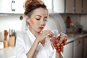Young beautiful Asian woman in beige lace shorts,white shirt eating grapes in the kitchen . selective focus: a small area of focus