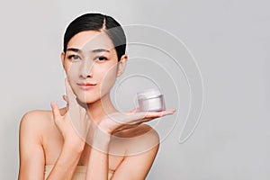 Young beautiful asian woman with clean, fresh and bright skin,holding Cream jar with positive emotional,isolated on gray