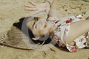 A young beautiful Asian woman dazzled by the light while lying on the beach sand