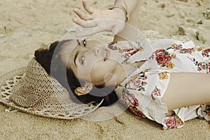 A young beautiful Asian woman dazzled by the light while lying on the beach sand