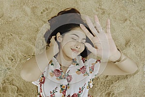 A young beautiful Asian woman dazzled by the light while lying on the beach sand