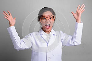 Young beautiful Asian woman doctor acting crazy while wearing novelty glasses