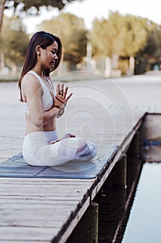 young beautiful asian woman doing yoga in a park. Sitting on the bridge with reflection on the water lake. Yoga and healthy