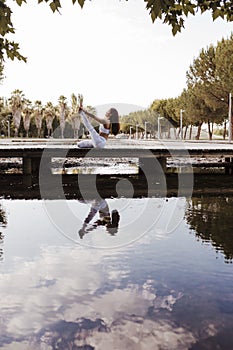 young beautiful asian woman doing yoga in a park. Sitting on the bridge with reflection on the water lake. Yoga and healthy