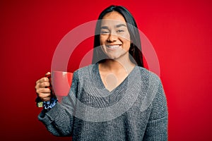 Young beautiful asian woman drinking mug of coffee standing over isolated red background with a happy face standing and smiling