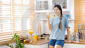Young beautiful asian woman drinking orange juice and smiling while standing by window in kitchen background, peolpe and healthy